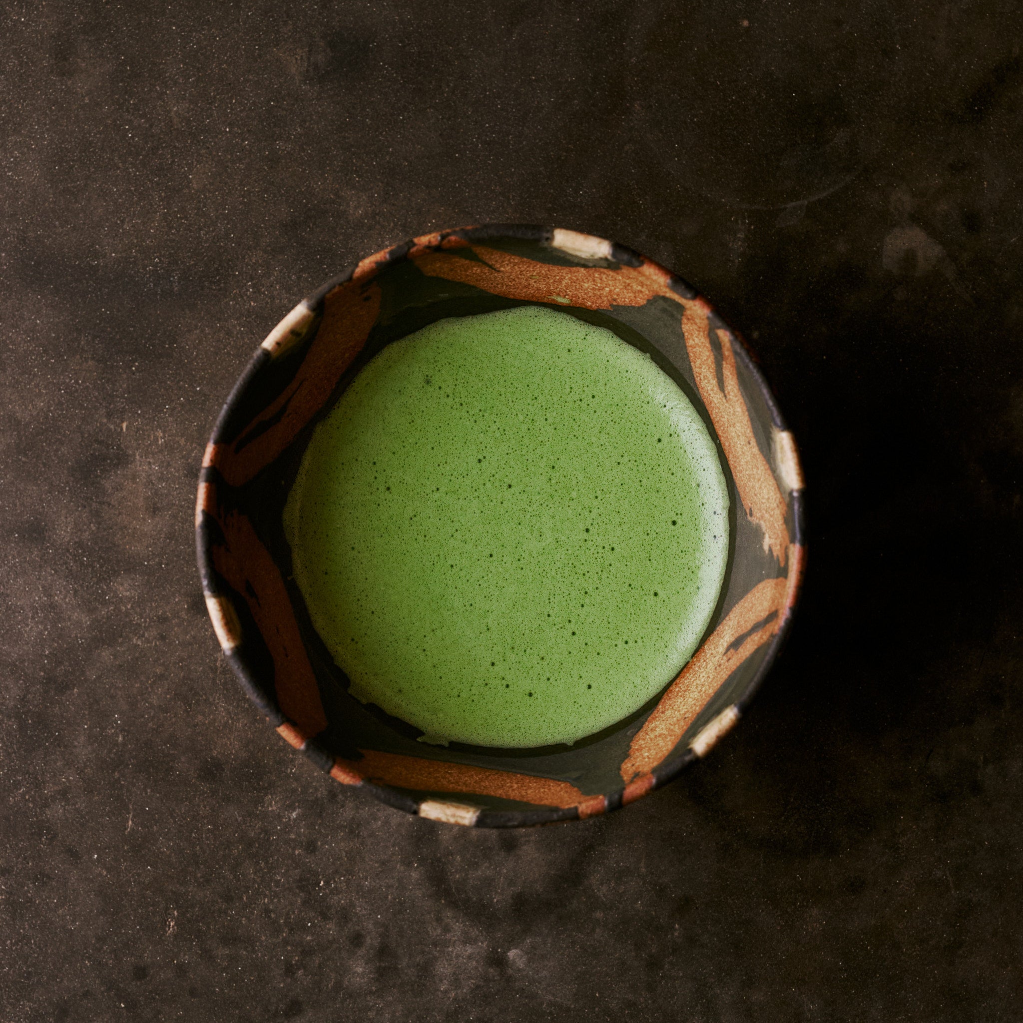 Matcha green tea in KUROMONMARU bowl - top view showing bold black and orange glaze pattern